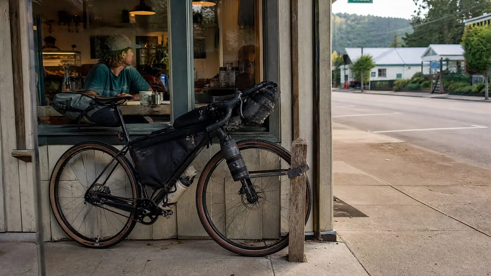 Loaded bikepacking bike secured to a wooden post outside a rural cafe with a compact band lock and a seatpost tracker